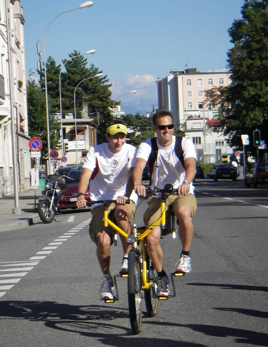 Matt Miller riding a tandem bike with another athlete on a city street.